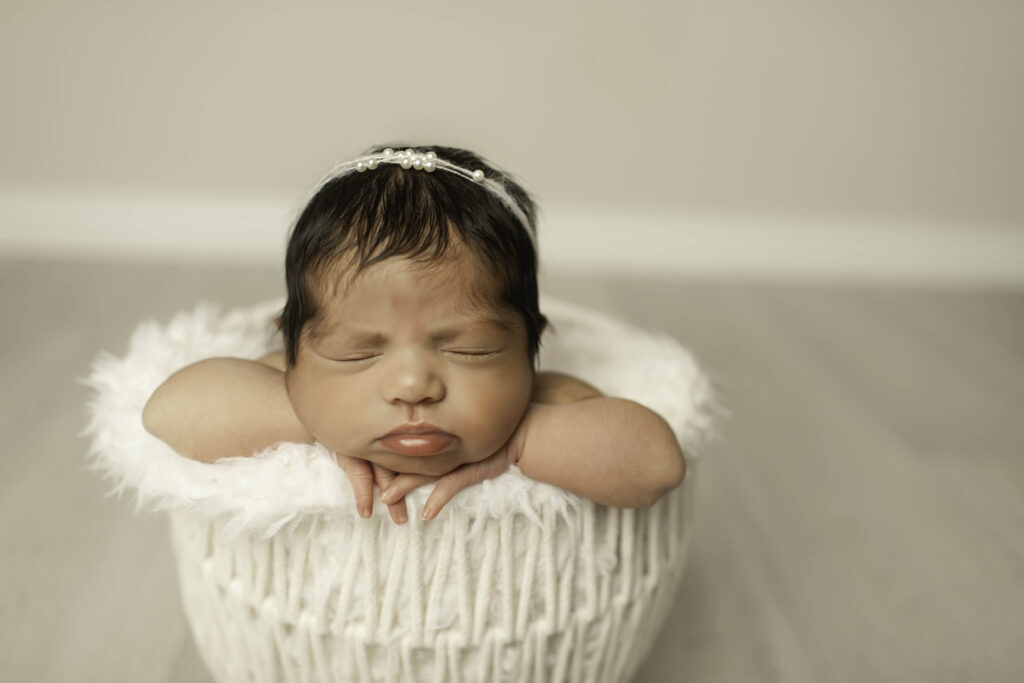 Wrapped in a cozy white blanket, a newborn girl rests peacefully in a white basket, her innocence and beauty highlighted in this timeless Fort Worth studio shot