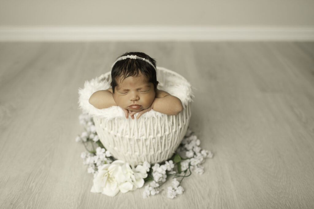 A newborn girl peacefully sleeps in a white basket, surrounded by soft blankets, her delicate features captured in a serene moment in a Fort Worth studio