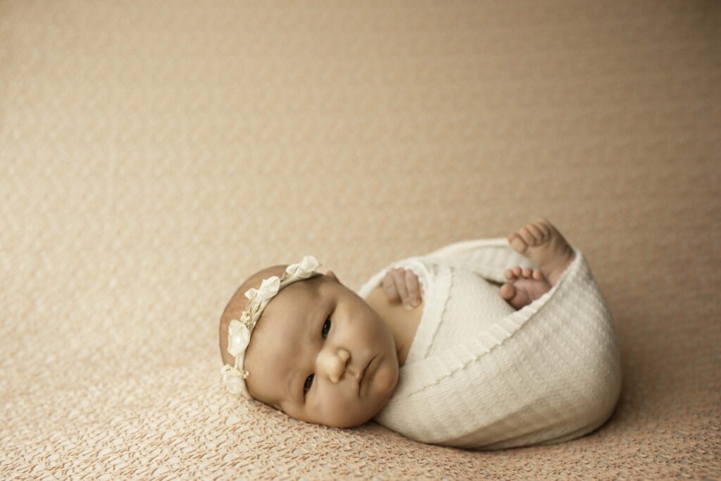 A newborn girl peacefully sleeps in a cozy blanket, her tiny hands gently tucked in, showcasing her innocence and calmness