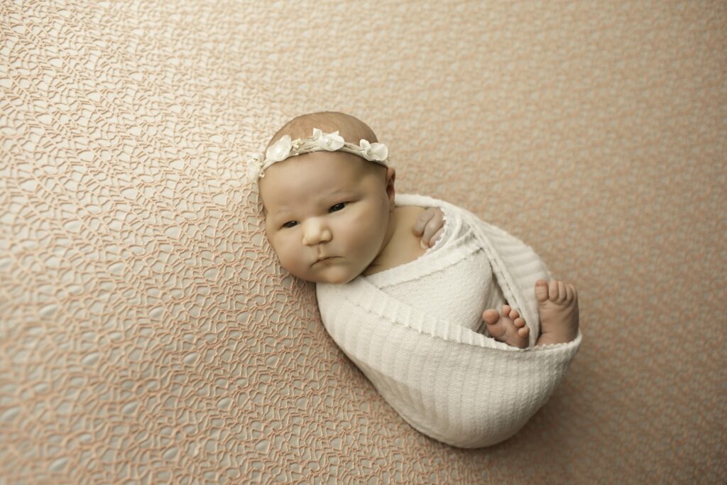 A sweet newborn girl lies on a soft, neutral blanket, with her tiny fingers resting peacefully beside her face in a serene pose