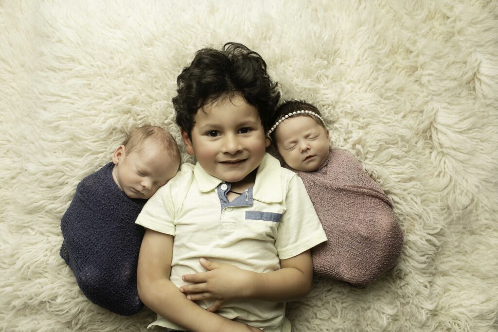 Big brother lovingly holding his newborn twin siblings in a heartwarming moment