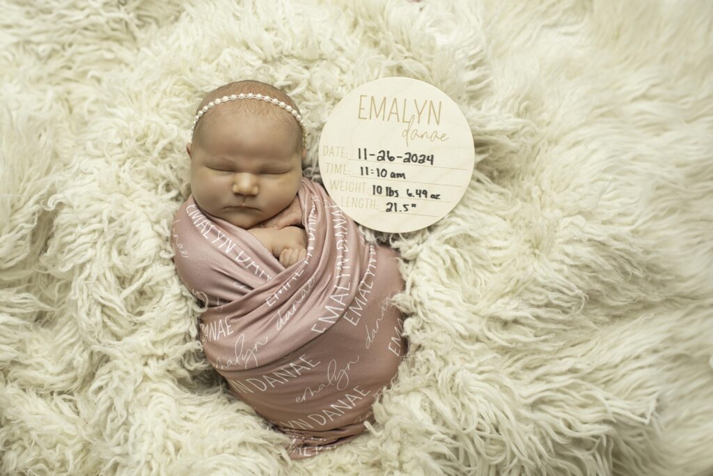 Wrapped in a personalized name blanket, a newborn with round, cherubic cheeks rests peacefully, creating a serene and heartwarming photoshoot moment.