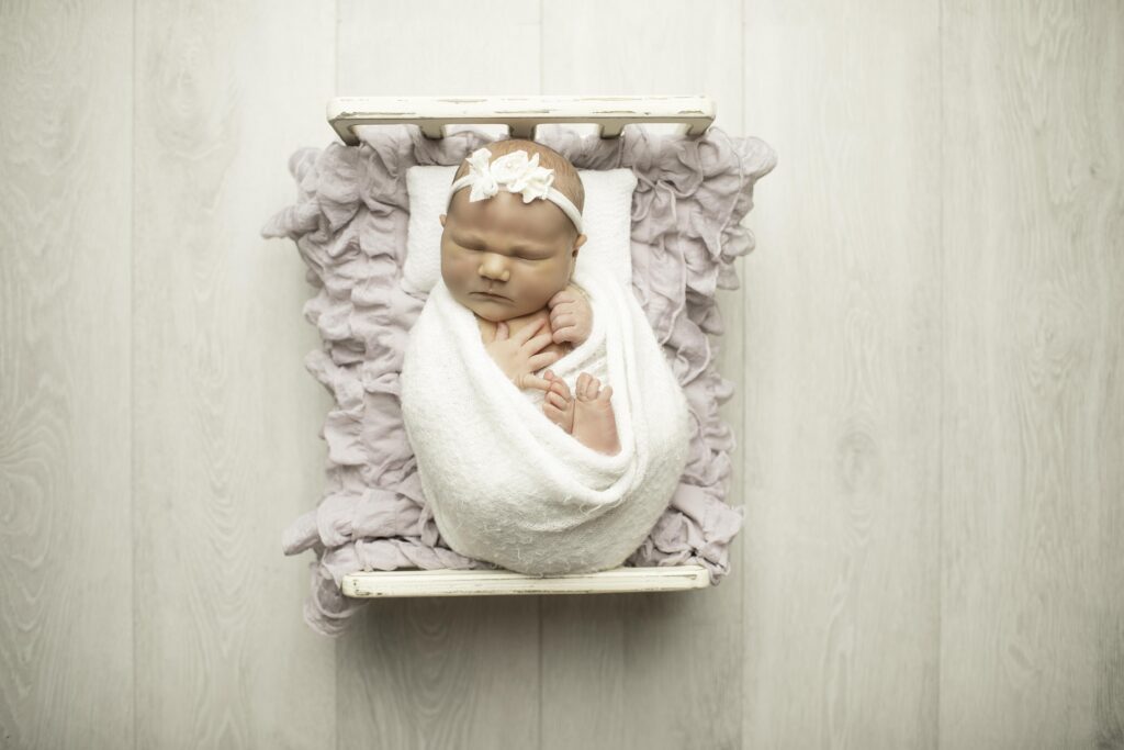 A newborn with plump cheeks is posed on a soft newborn bed, curled up peacefully in a warm, plush blanket, showcasing pure serenity