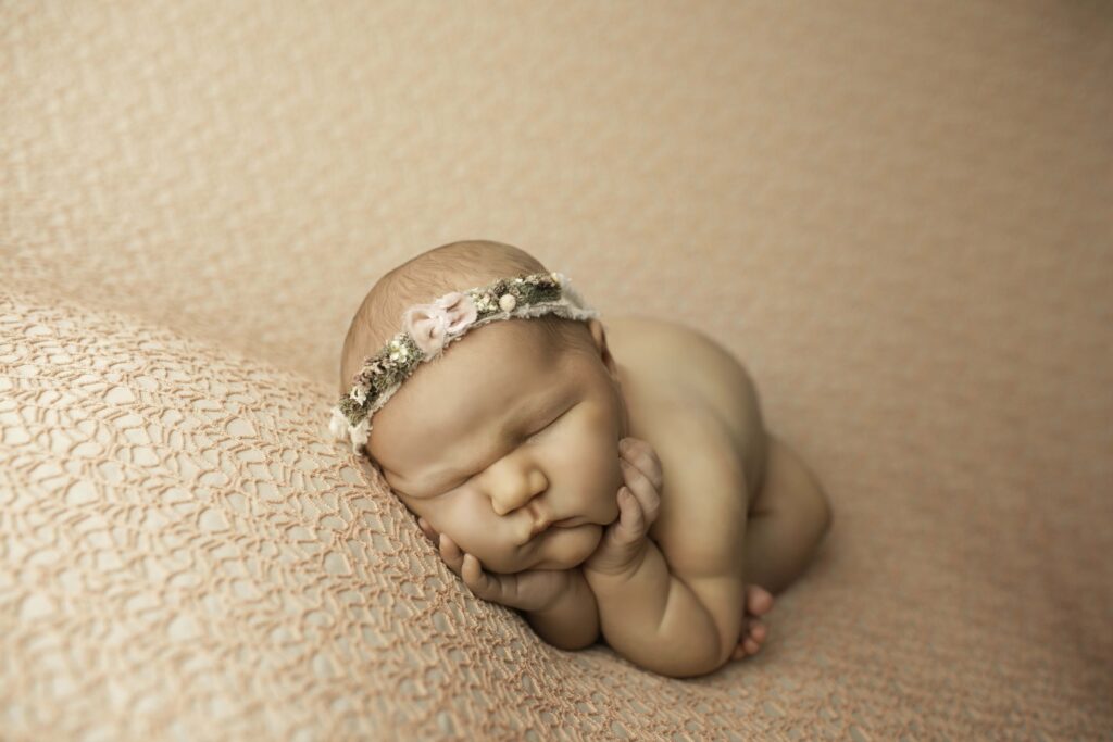 A newborn baby with round, chubby cheeks looks peacefully asleep, with a tiny hand resting near their face, showcasing pure innocence