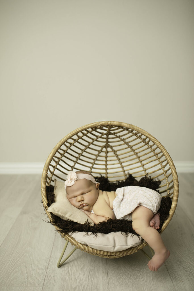 A newborn with chunky cheeks lies on their tummy in a wicker basket, wrapped in a soft, neutral blanket, exuding peacefulness and charm