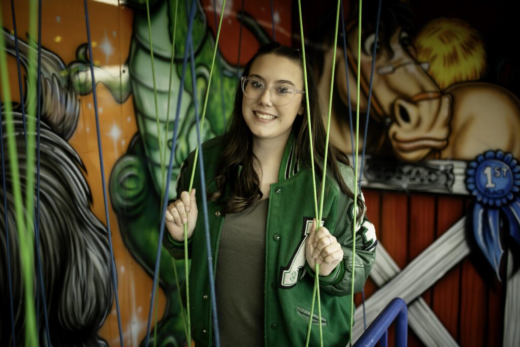 Senior girl mid-laugh while navigating a wobbly bridge inside a funhouse game at the Stockshow Midway.
