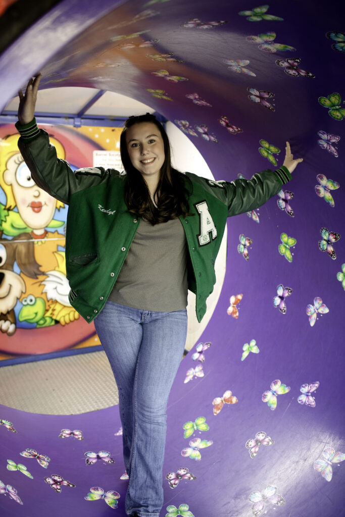 Senior girl stepping carefully through a spinning tunnel in a walk-through carnival game, holding onto the rail and smiling.