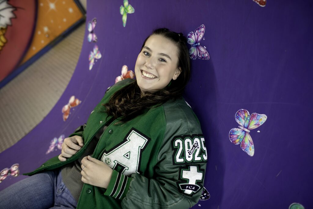 Senior girl laughing as she walks through a colorful funhouse game with mirrors and bright lights around her.