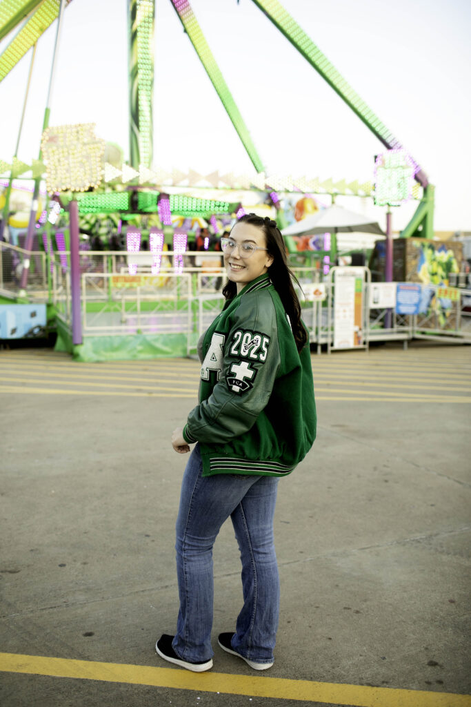 Senior girl smiling brightly in front of colorful game booths at the Fort Worth Stockshow Midway.