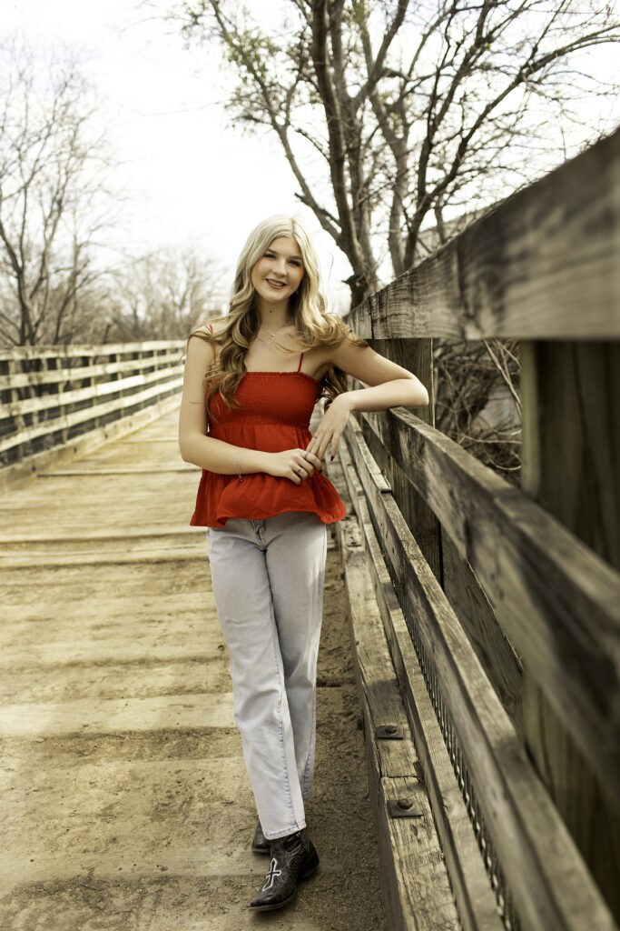 Senior girl in red shirt laughing while standing in the middle of a wooden bridge at the Stockyards Cactus Garden.