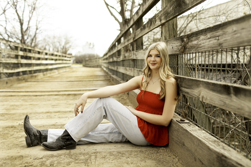 Senior girl walking across a rustic bridge in a red shirt, with cacti and desert textures in the background.