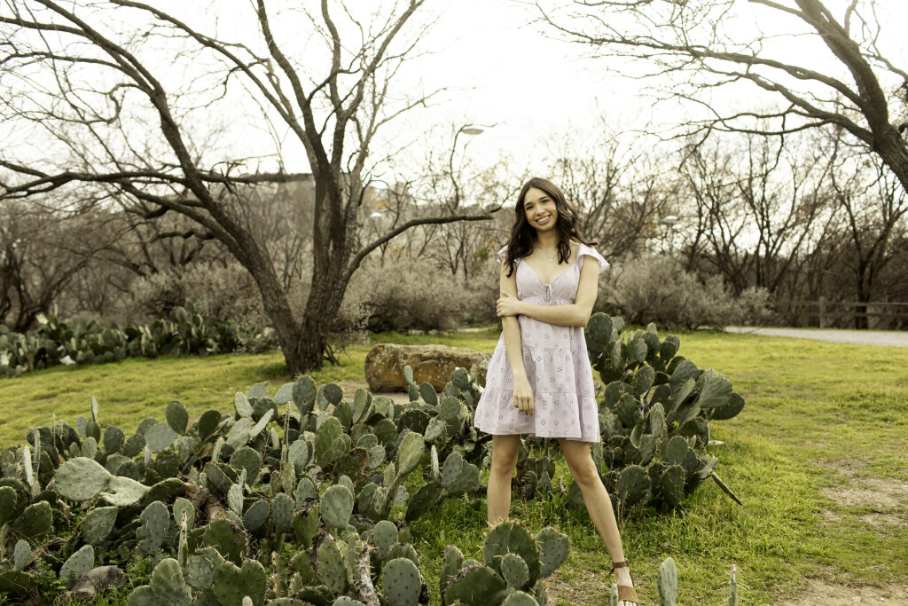 Senior girl walking towards the camera through the cactus garden, with her head tilted slightly and a soft smile.
