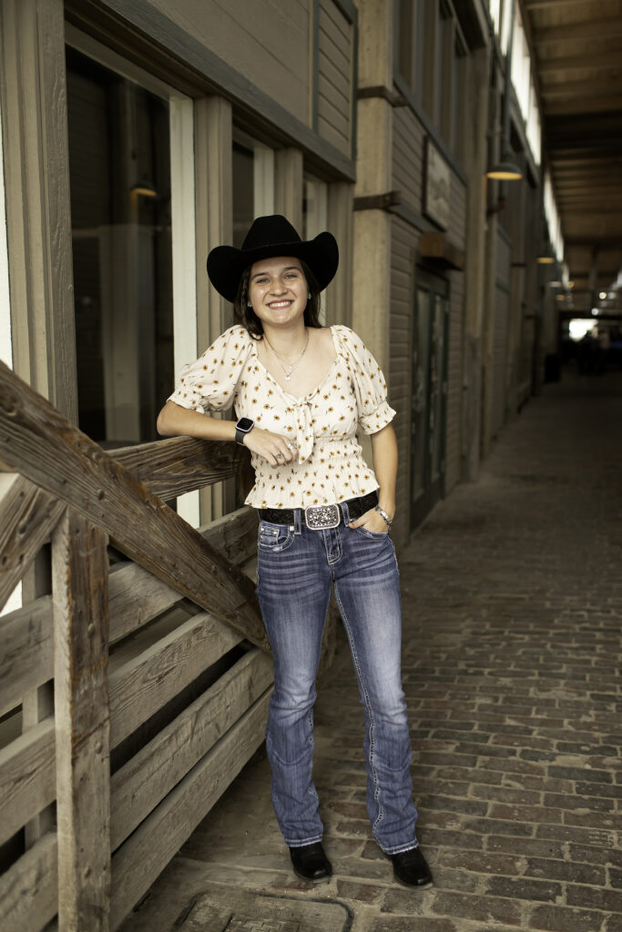 Close-up of senior girl with the rustic wooden fences of the Stockyards as the backdrop, showing off her casual style.