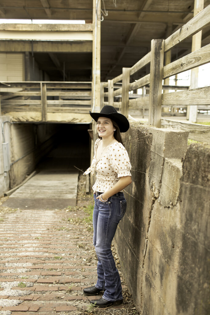 Senior girl standing on the cobblestone street at the Fort Worth Stockyards, with rustic buildings in the background.