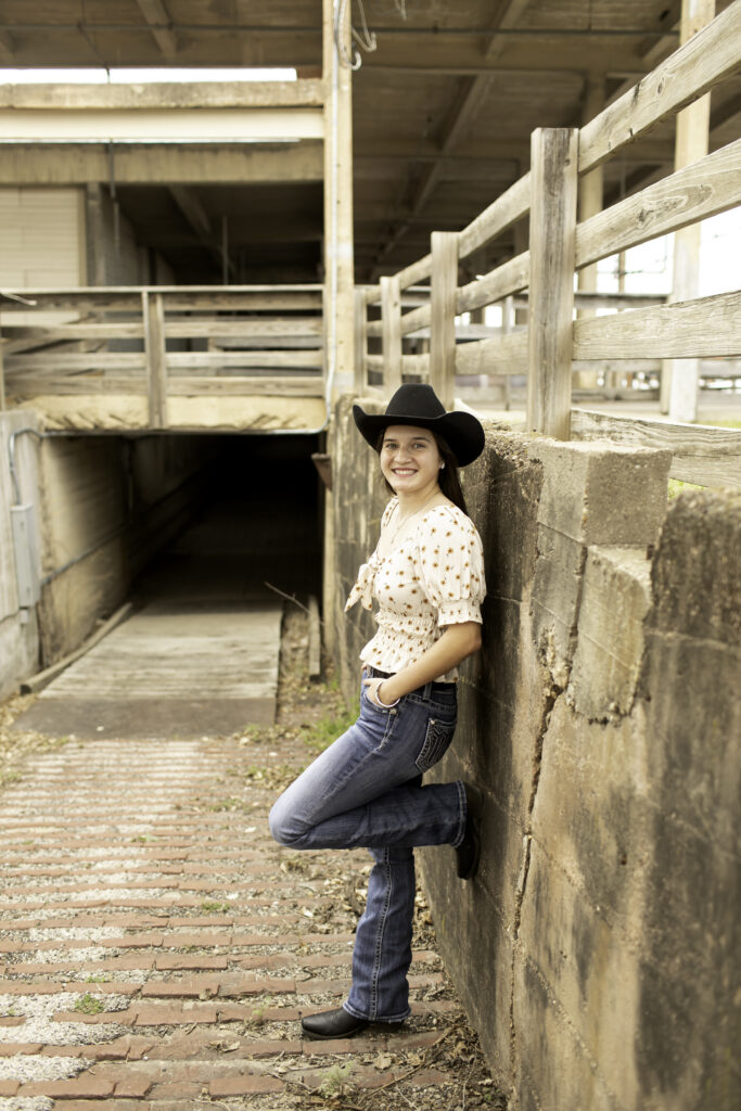 Senior girl standing on the cobblestone street at the Fort Worth Stockyards, with rustic buildings in the background.