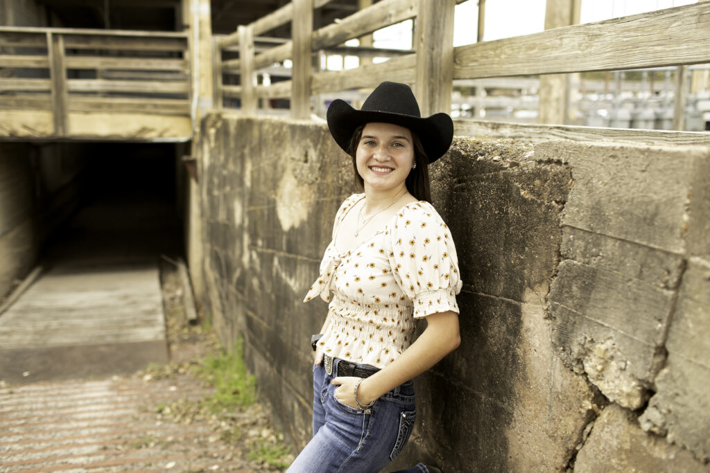 Senior girl standing on the cobblestone street at the Fort Worth Stockyards, with rustic buildings in the background.