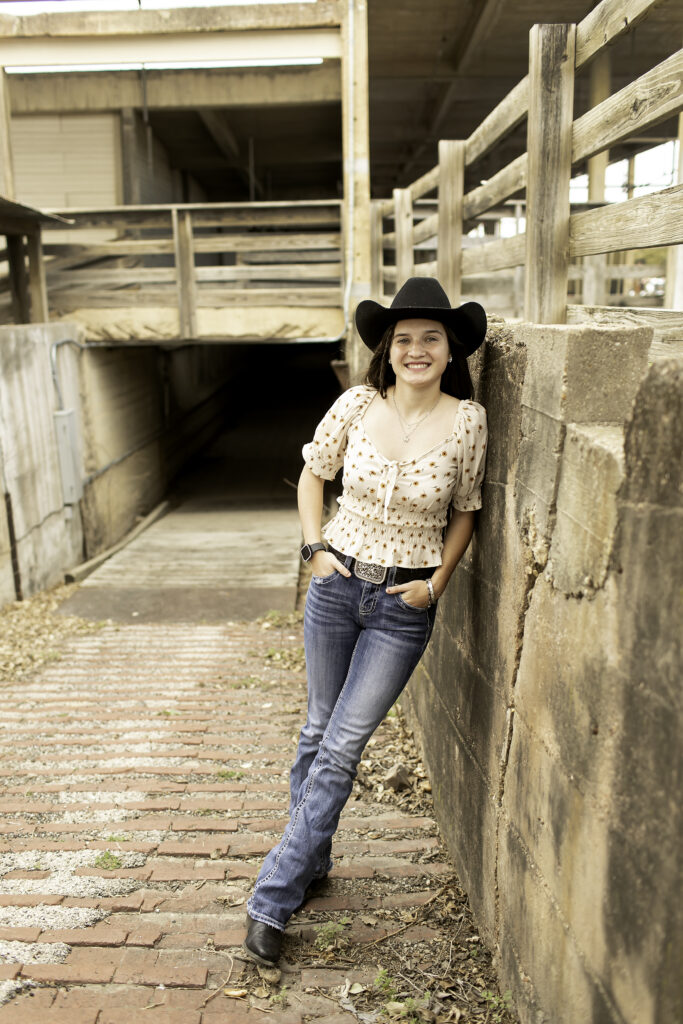 Senior girl standing on the cobblestone street at the Fort Worth Stockyards, with rustic buildings in the background.