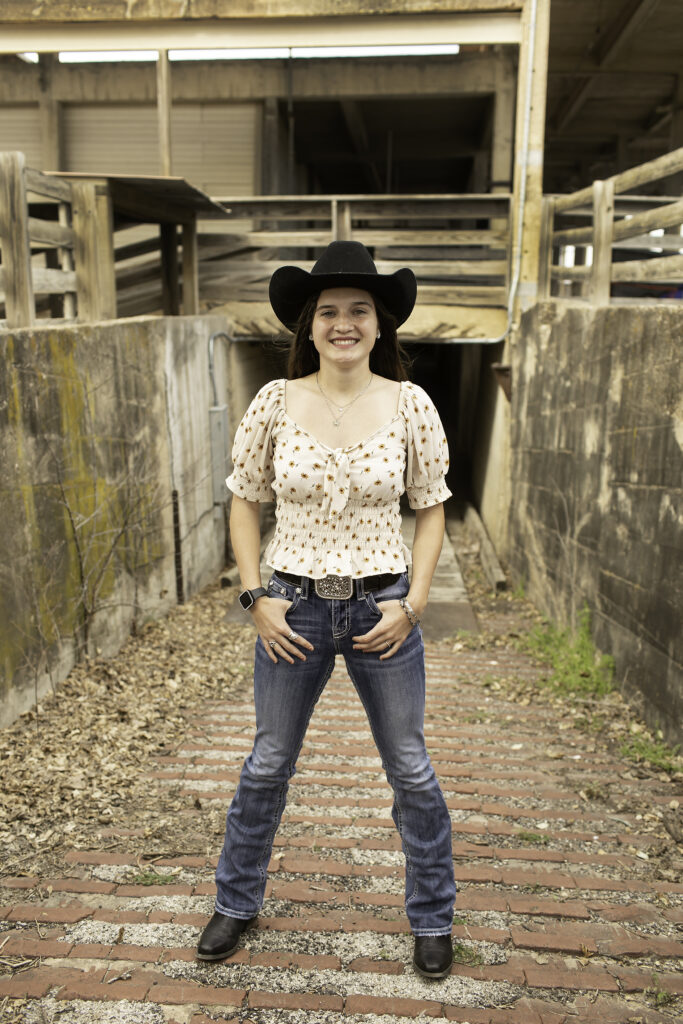 Senior girl standing on the cobblestone street at the Fort Worth Stockyards, with rustic buildings in the background.
