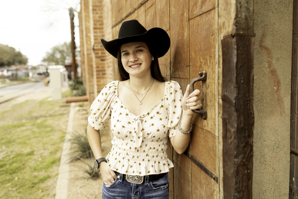 Senior girl leaning against a weathered brick wall in the Fort Worth Stockyards, with sunlight casting a warm glow on her.