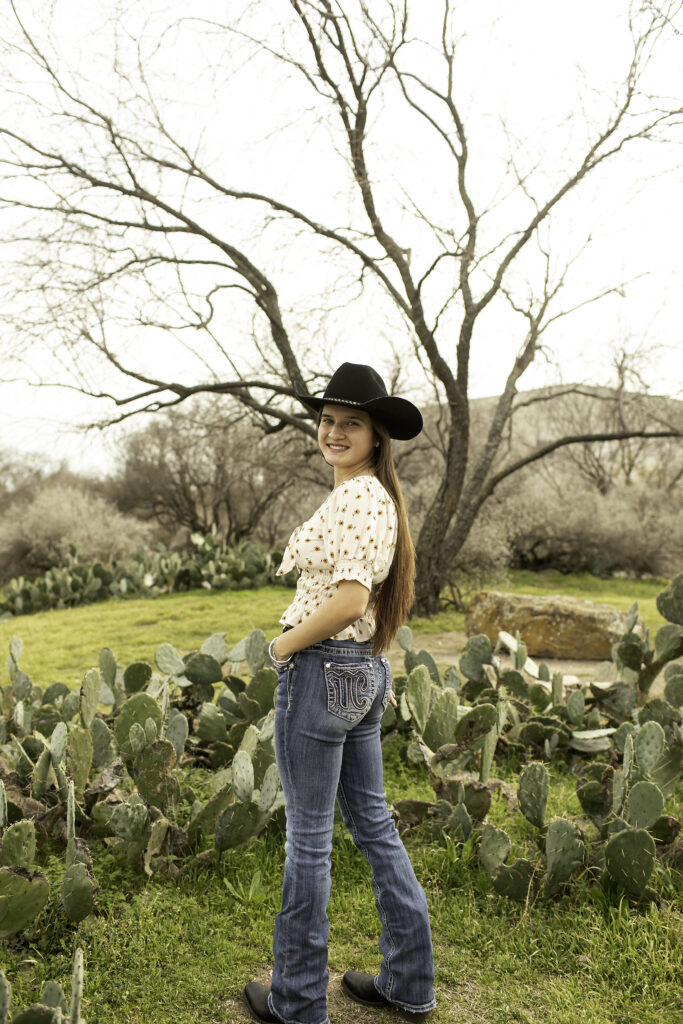 Full-body shot of a senior girl standing in the Cactus Garden, her flowing dress contrasting with the rugged plants.