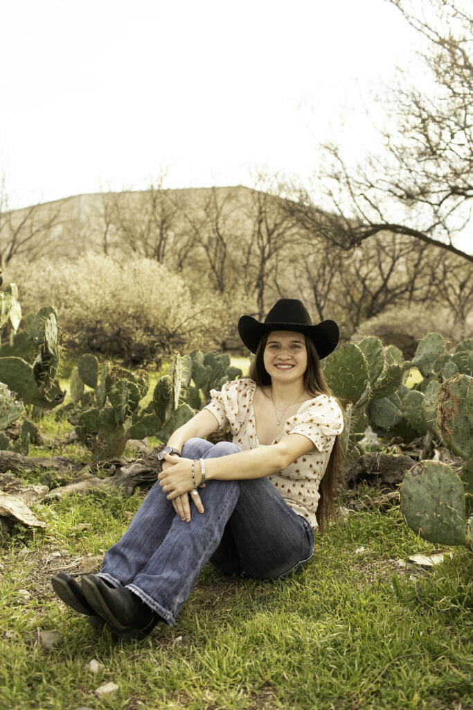 Close-up shot of a senior girl with a soft smile, framed by the desert plants in the Cactus Garden.
