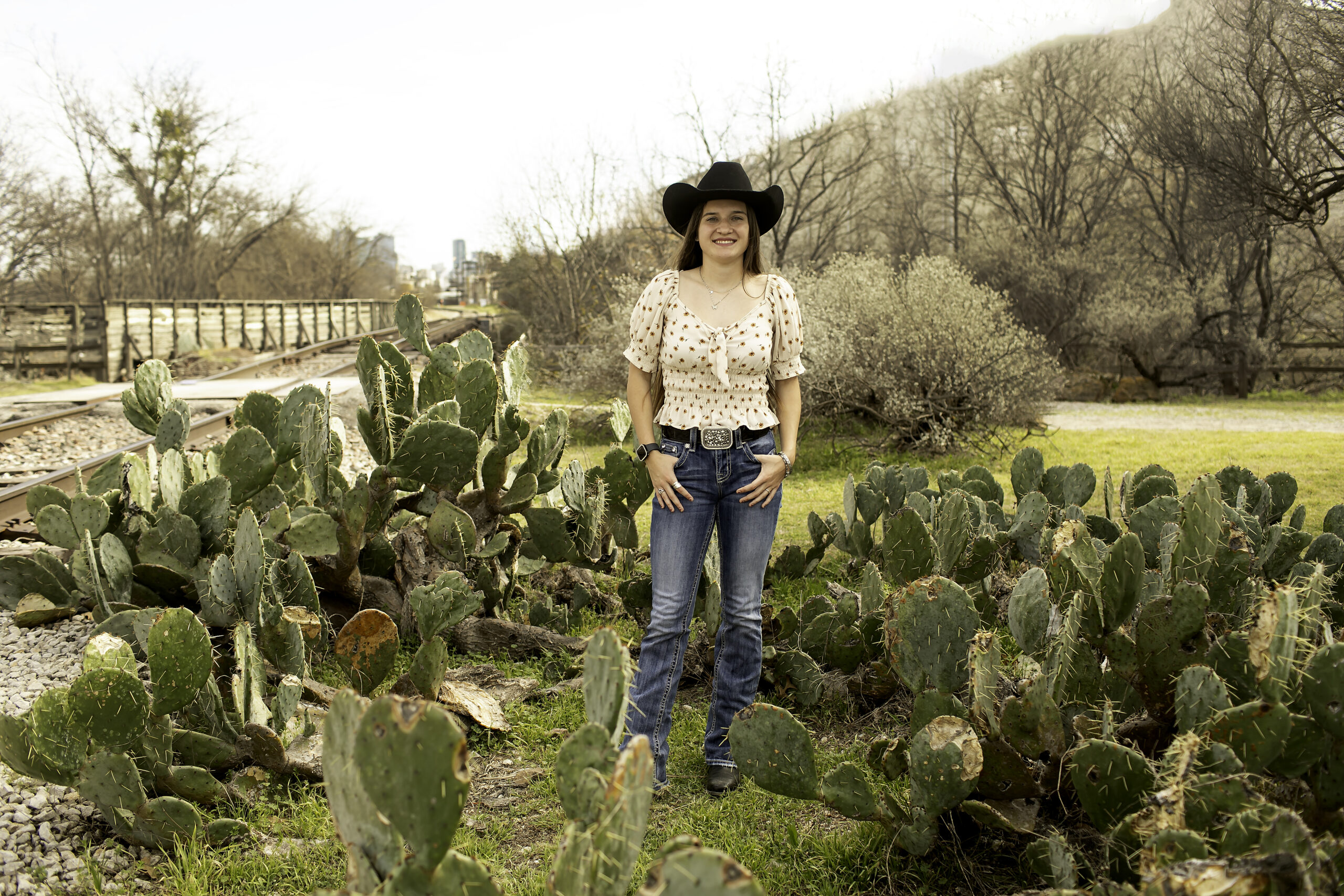 Senior girl smiling in front of tall cacti in the Cactus Garden at the Fort Worth Stockyards.