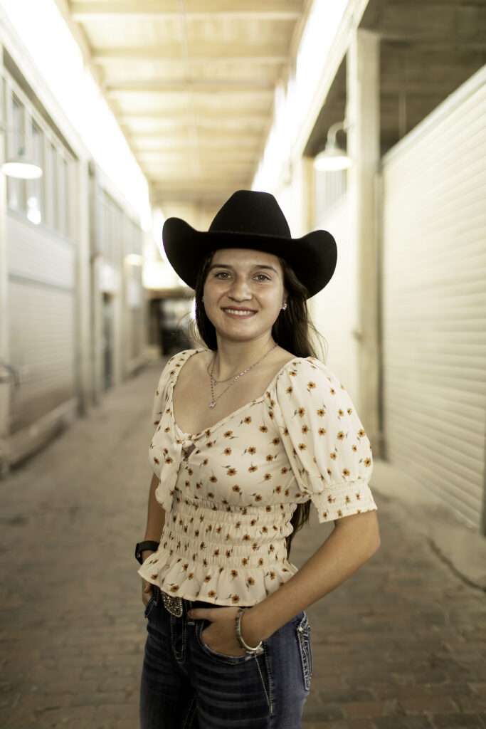 Senior girl smiling and posing in front of the Western shops at the Stockyards, with the wooden storefronts in the background.