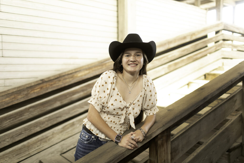 Senior girl with a relaxed pose, standing next to an old Western-style horse corral at the Stockyards.