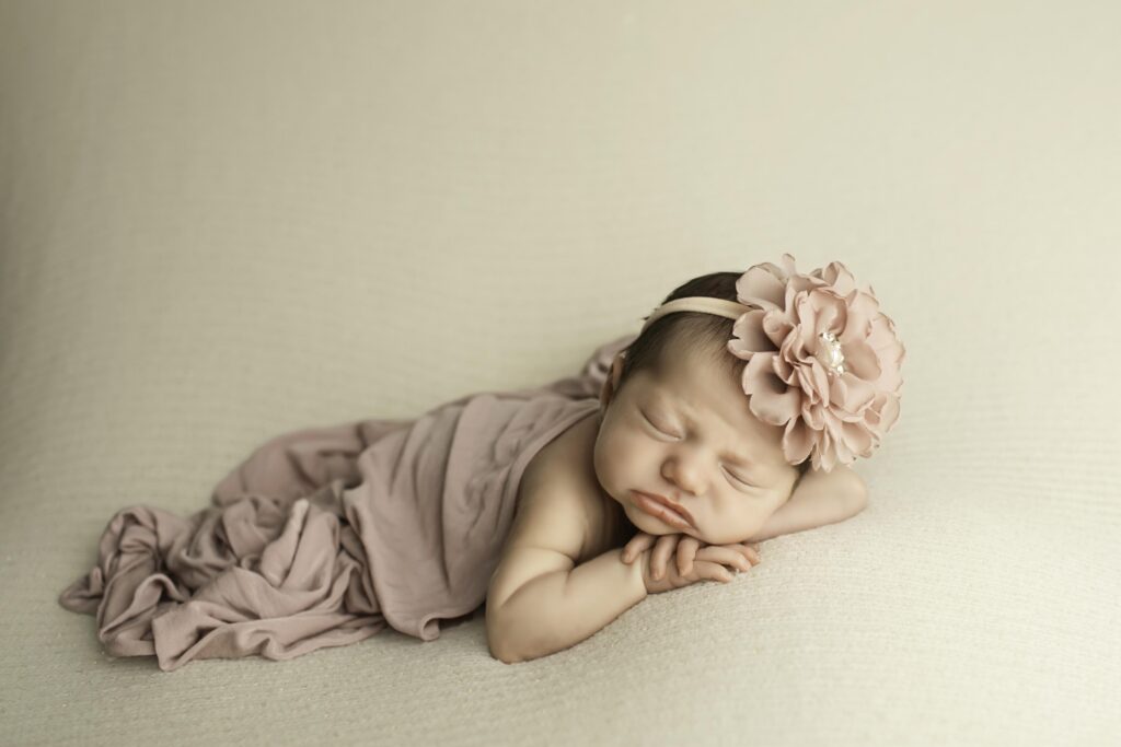 Newborn posed with chin resting gently on her wrist, lying belly-down on a soft white background.