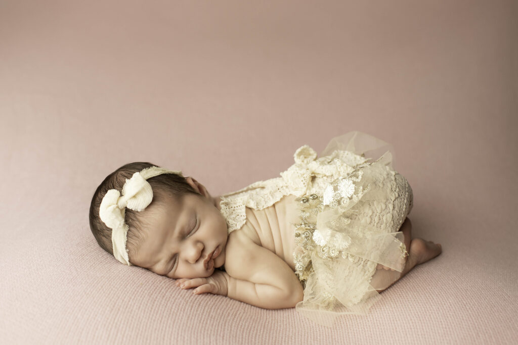 Curled-up newborn girl in the womb pose on a solid pink blanket, arms and legs tucked in close for a cozy look.