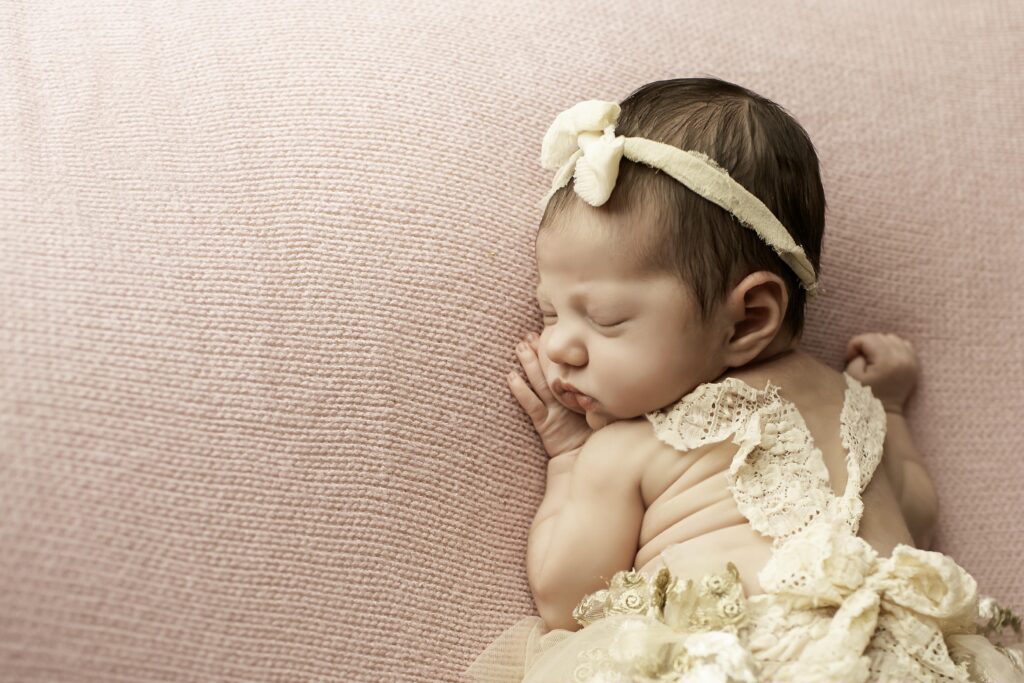 Curled-up newborn girl in the womb pose on a solid pink blanket, arms and legs tucked in close for a cozy look.