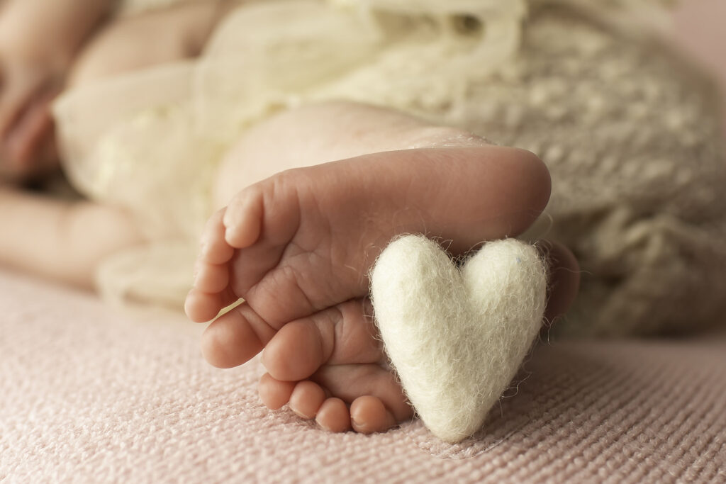 Close-up of tiny newborn feet resting on a soft blanket, with a small felt heart gently placed on the toes.