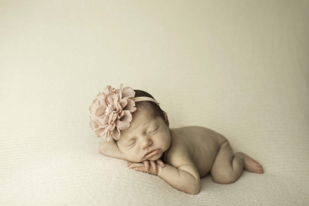 Newborn posed with chin resting gently on her wrist, lying belly-down on a soft white background.