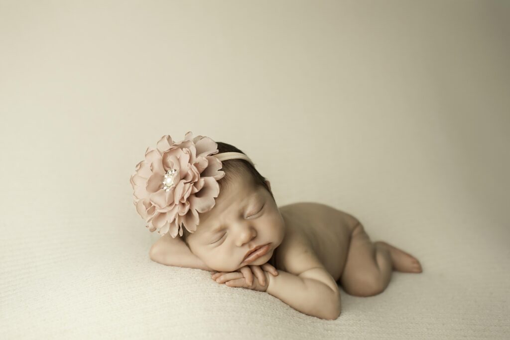 Newborn posed with chin resting gently on her wrist, lying belly-down on a soft white background.