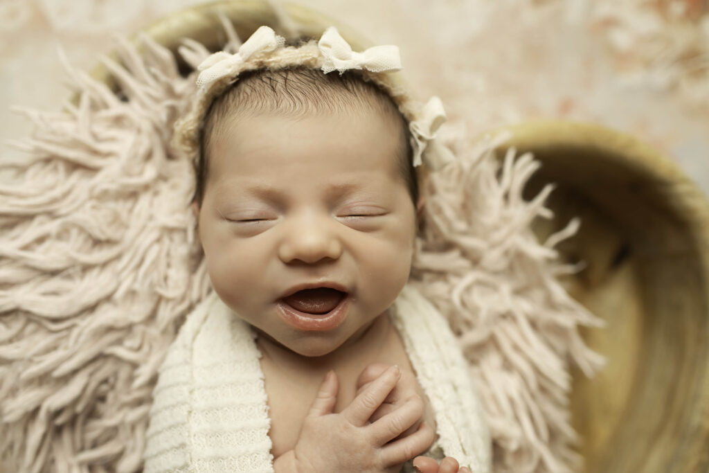 Newborn girl peacefully swaddled in a soft cream-colored blanket, resting in a heart-shaped prop adorned with a delicate lace trim, set against a neutral-toned backdrop.