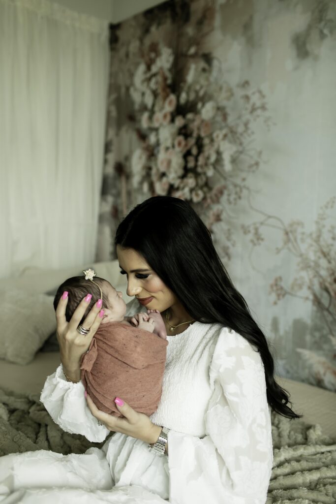 Mom holding her newborn daughter close, surrounded by soft linens and boho-inspired decor in a serene nursery setting.