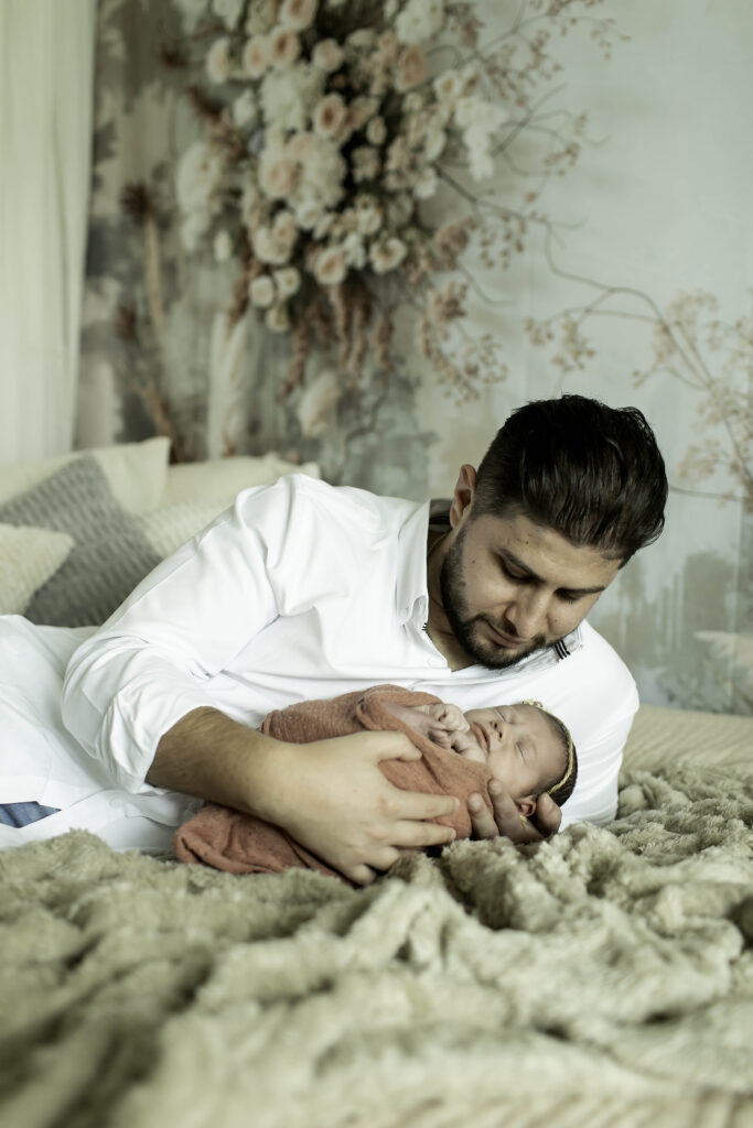 Father cradling his newborn girl in a cozy boho nursery, with a woven bassinet and macramé wall hanging in the background.