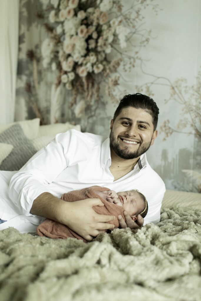 Dad gently holding his newborn daughter in a boho-inspired nursery, surrounded by soft textures and neutral tones