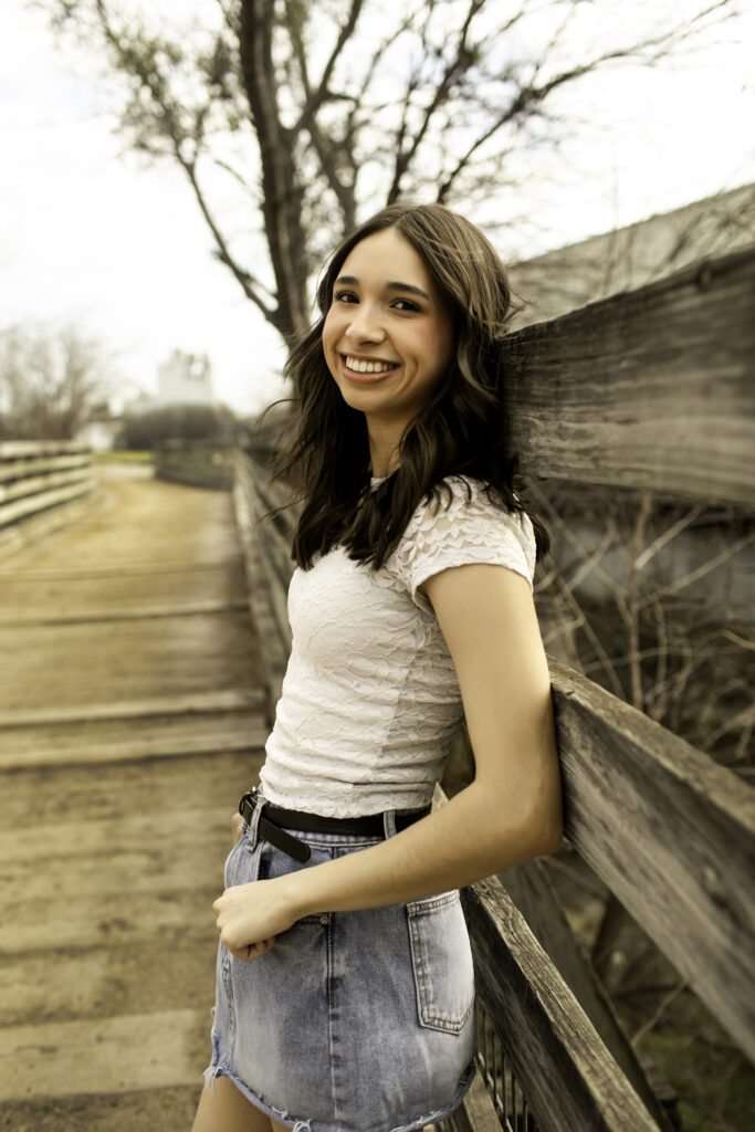 Senior girl standing on a wooden bridge in the Cactus Garden at the Fort Worth Stockyards, smiling with the desert plants surrounding her.