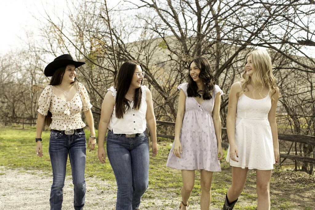 Group of four senior girls holding hands and walking across a weathered wooden bridge, showing off their team spirit.