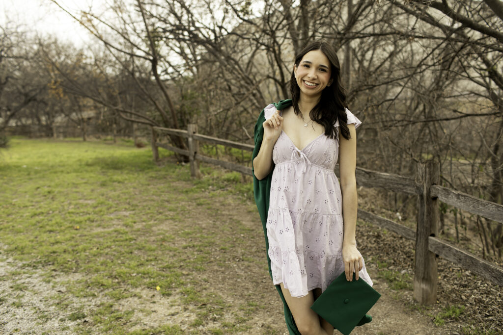 Senior girl with her arms resting on a rustic fence, surrounded by the natural textures of wood and desert greenery.
