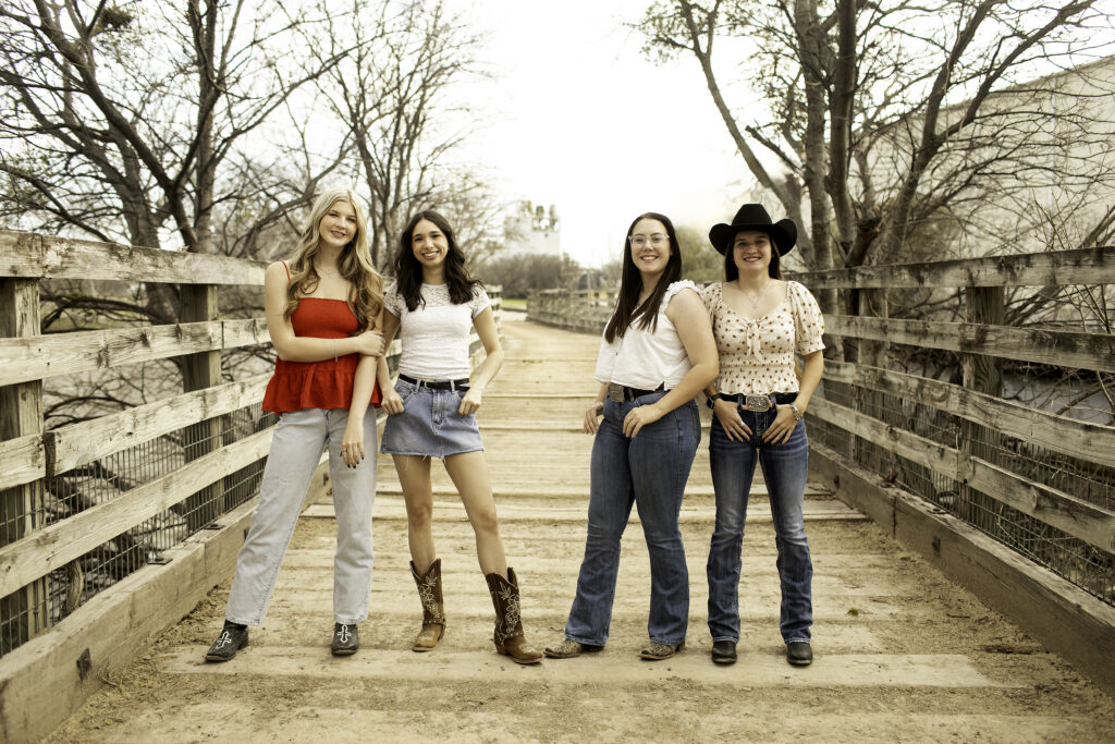Senior rep team of four girls standing in a relaxed pose on a wooden bridge, surrounded by natural greenery and charm.