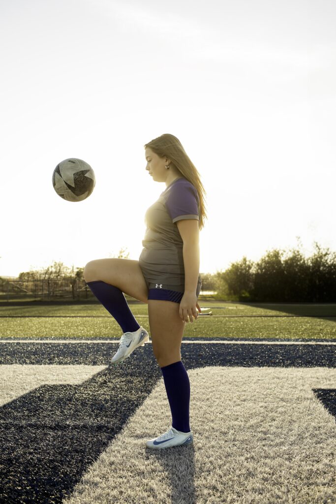 Teen soccer athlete performing a knee juggle, demonstrating skill and precision on the field.