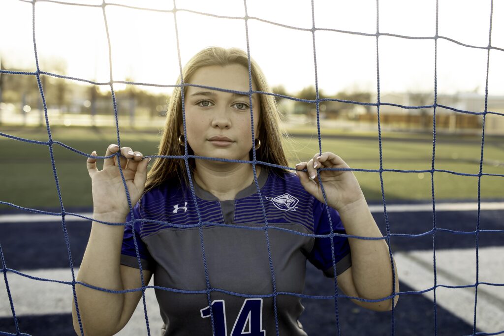 Soccer player standing in front of the net, arms crossed and cleats dug into the turf.