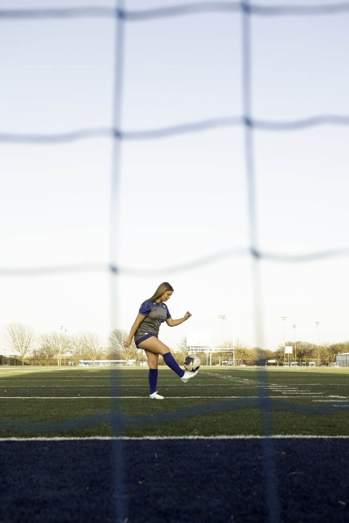 High school soccer player dribbling the ball across the field, eyes focused ahead, showcasing agility and control.