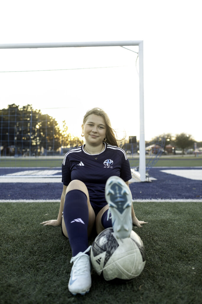 Soccer player in uniform posing with one foot on the ball, looking fierce under the stadium lights.