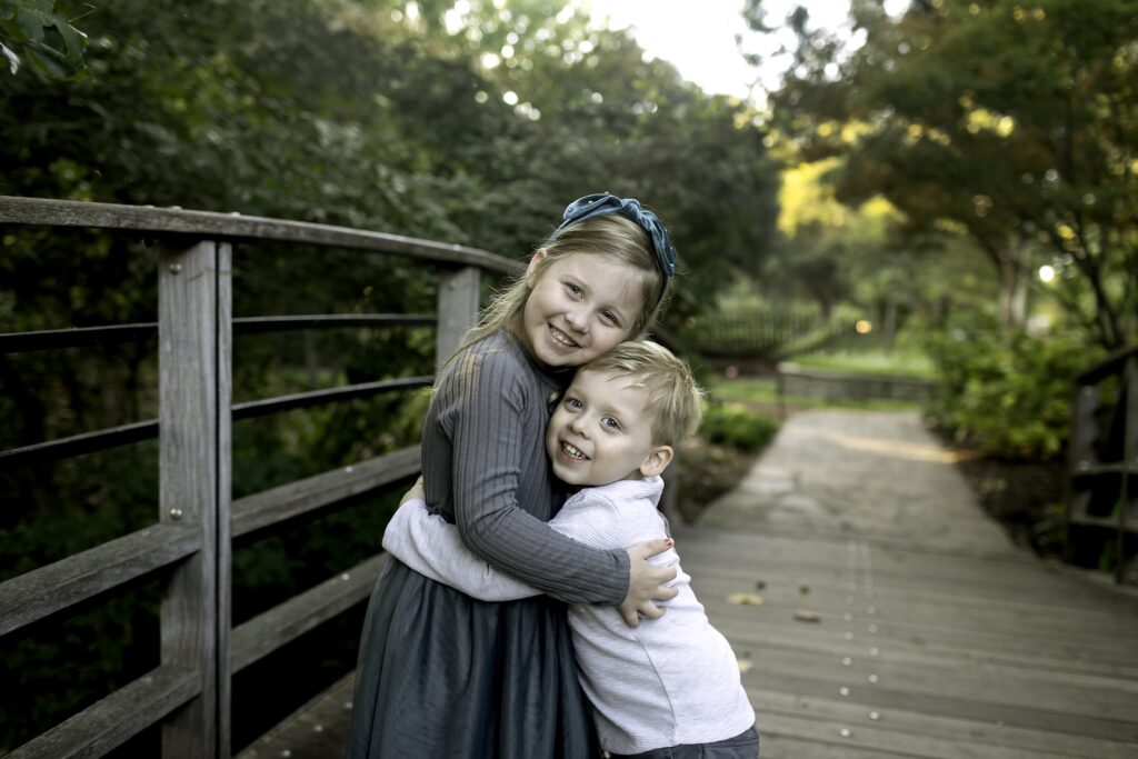 Brother and sister sitting side by side on a garden bench, smiling at the camera