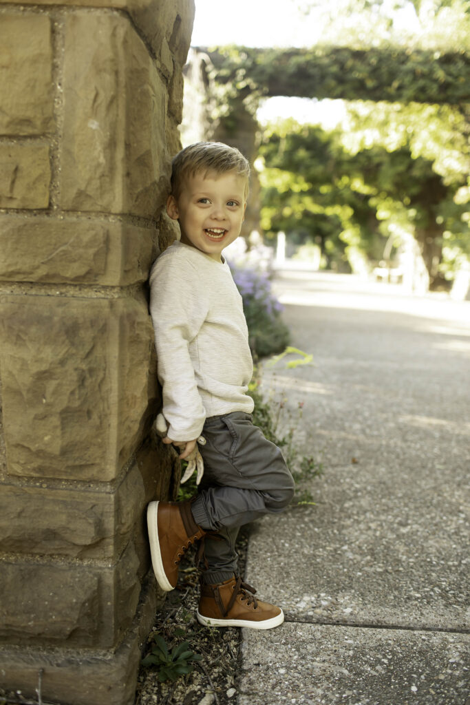 Close-up of brother smiling shyly at the camera with the gardens behind him