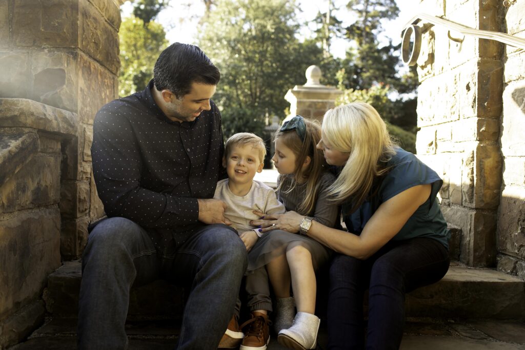 Casual shot of the family sitting together on the steps of a garden gazebo, all smiling