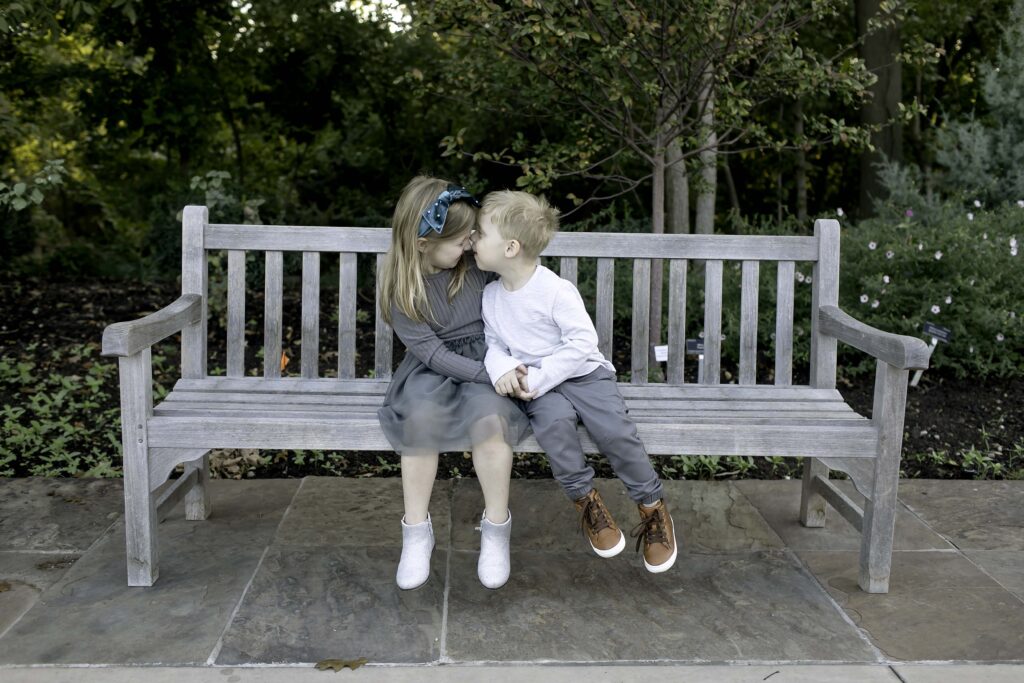 Sweet hug between brother and sister as they sit on a bench surrounded by flowers